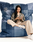 Femme assise sur le bean bag Osmoze à carreaux bleu, café à la main, détente au chalet